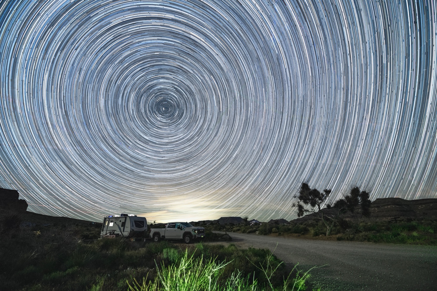 Long-exposure star trails circling above a desert camp in the Mojave